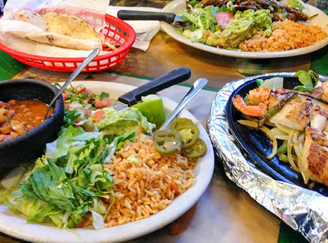 Several plates of food on a table. Fajutas, rice and beans, fish tacos