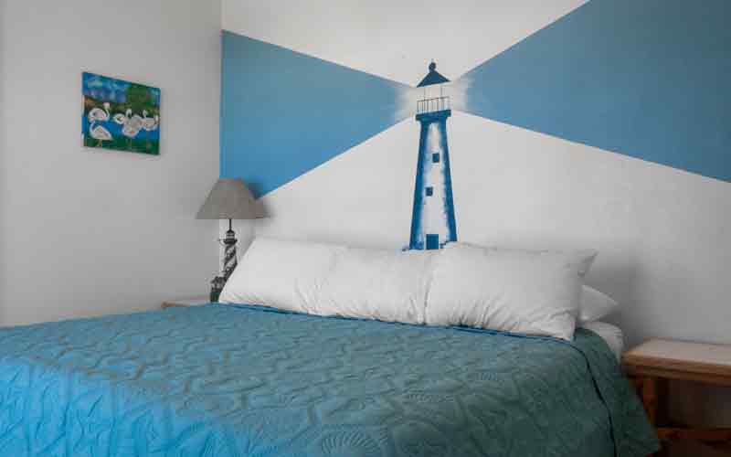 Bedroom in Unit 9, Sandollar Sity Vacation Rentals in Port Aransas, Texas. Painting of lighthouse on wall behind bed.