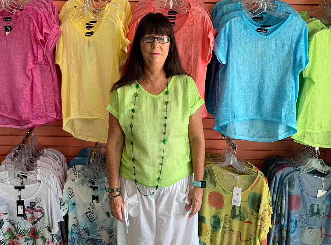 The owner of Island Woman Boutique standing in front of a wall of colorful blouses