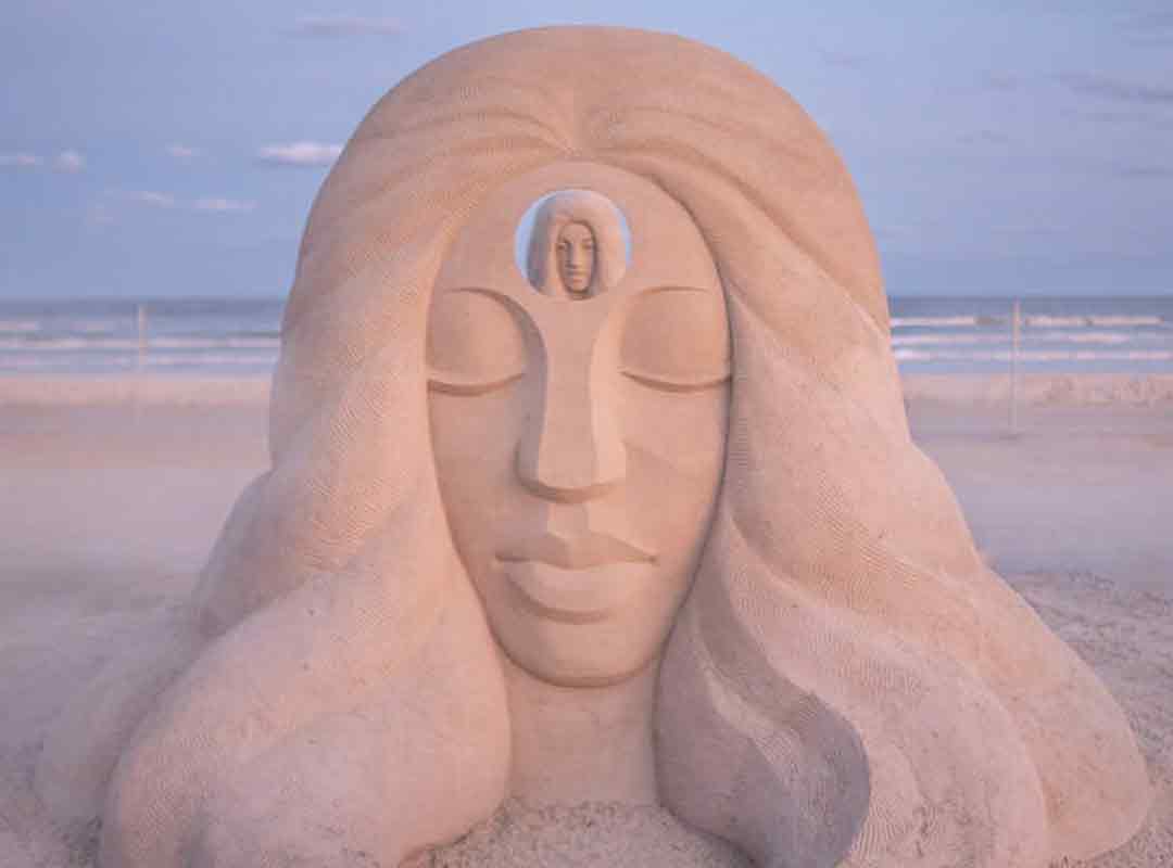 Sand Sculpture of woman's head. There is a hole in the head where you can see another sculpture behind this one.